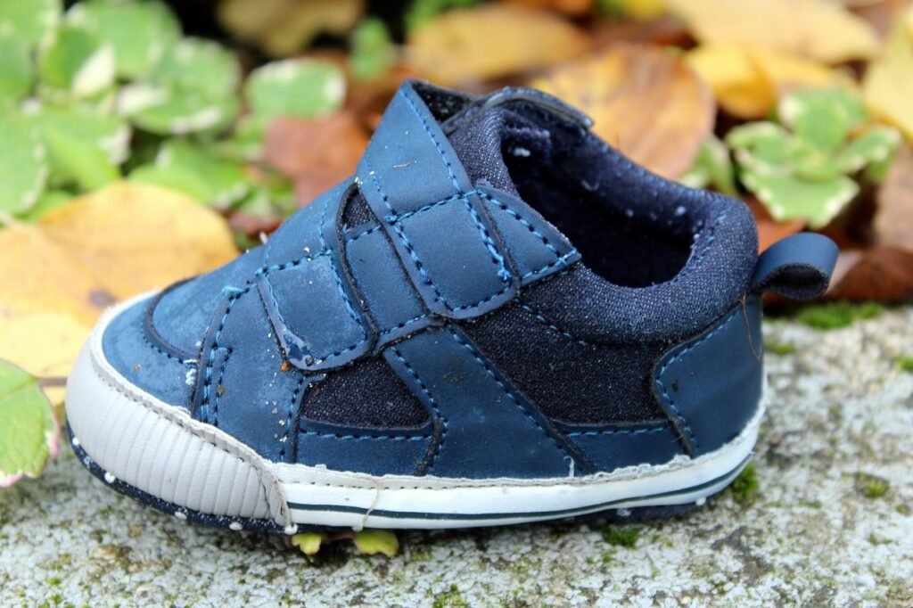 Zapato infantil azul con velcro, usado y algo desgastado, sobre una piedra entre hojas de otoño