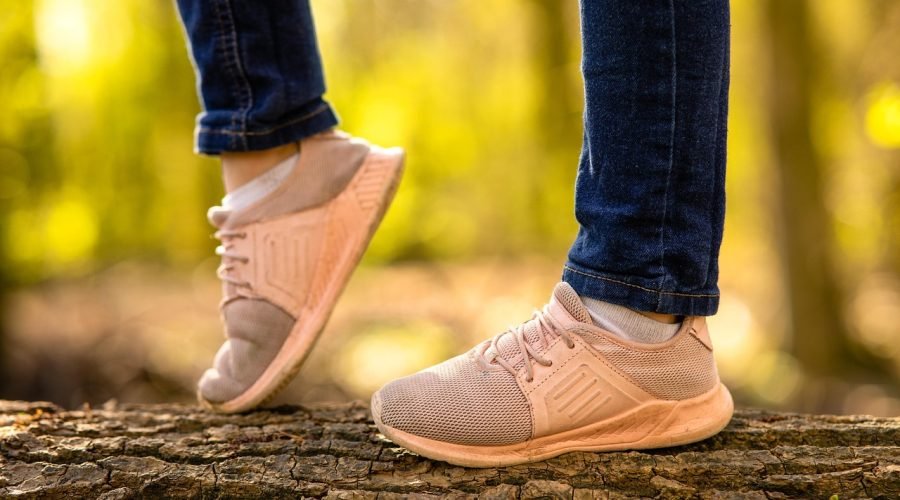 Pies de un niño con zapatillas deportivas caminando sobre un tronco en el bosque