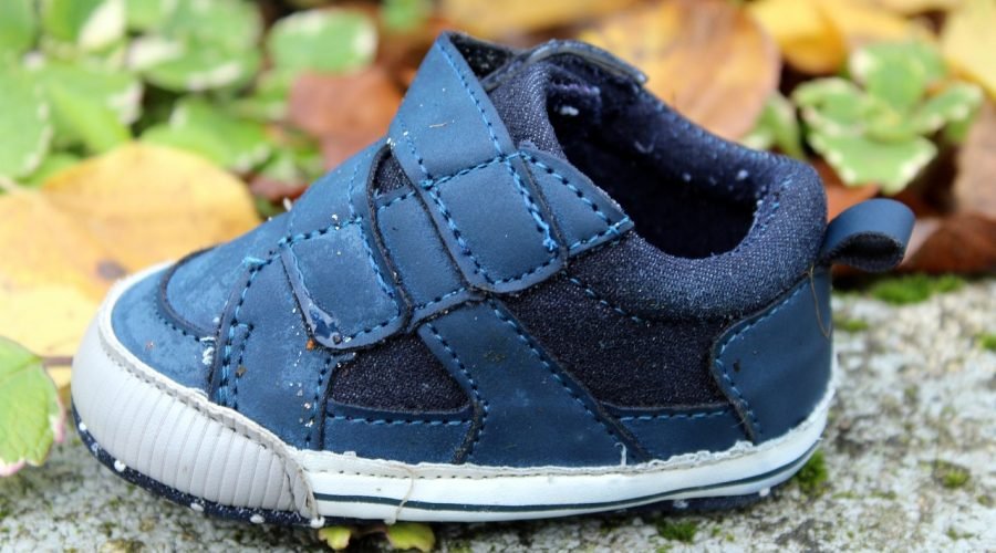 Zapato infantil azul con velcro, usado y algo desgastado, sobre una piedra entre hojas de otoño