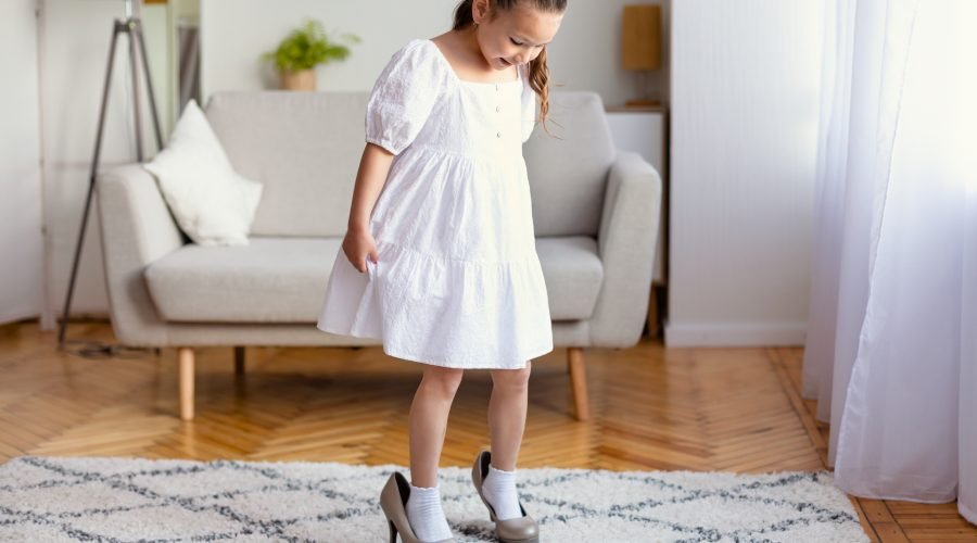 Beautiful Little Girl Wearing Mom's High Heels Shoes Playing At Home. Kid's Fashion, Clothing And Style Concept